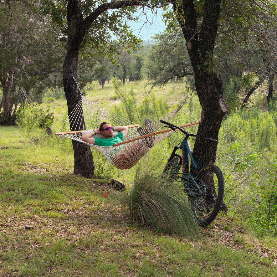 A man relaxes in a hammock with his mountain bike resting against a tree.